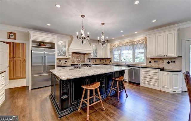 kitchen featuring a kitchen island with sink, appliances with stainless steel finishes, a sink, white cabinetry, and a notable chandelier