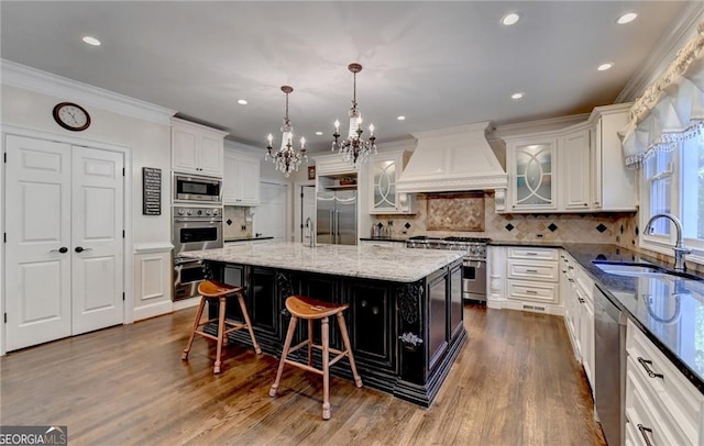 kitchen with white cabinetry, a sink, built in appliances, an inviting chandelier, and custom exhaust hood
