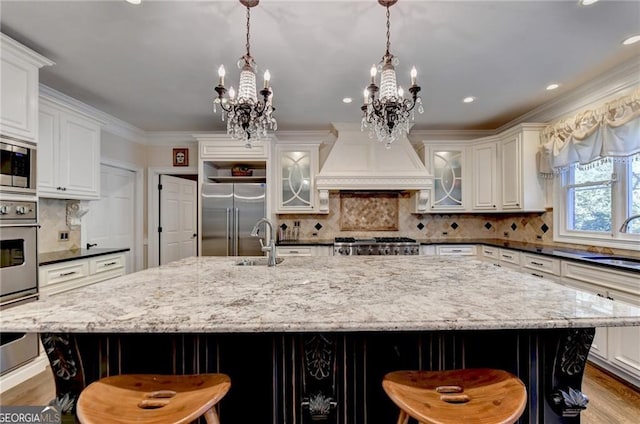 kitchen featuring a chandelier, custom range hood, built in appliances, a sink, and white cabinetry