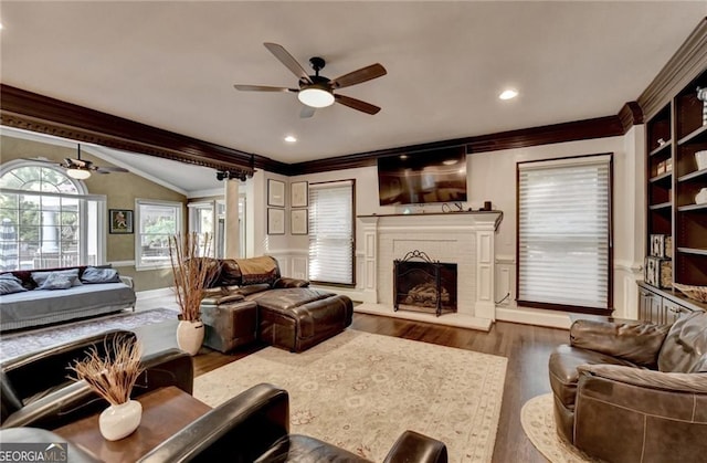living area with ornamental molding, a ceiling fan, a brick fireplace, and wood finished floors