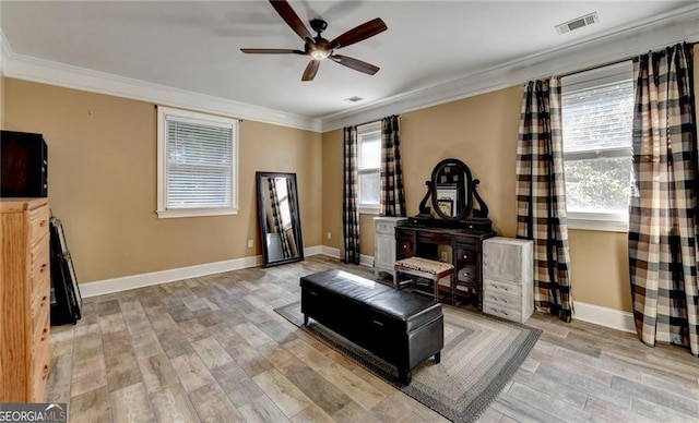 living area featuring wood finished floors, baseboards, visible vents, a ceiling fan, and crown molding