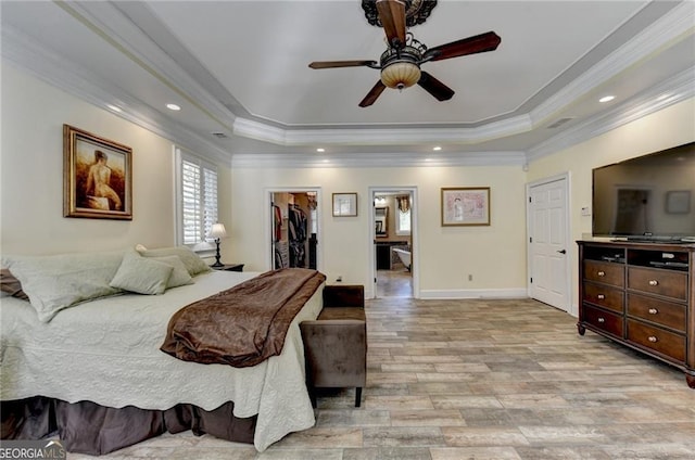 bedroom featuring crown molding, light wood finished floors, a raised ceiling, and a spacious closet