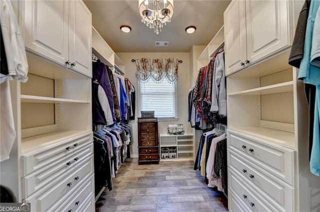 spacious closet featuring wood finished floors, visible vents, and a notable chandelier