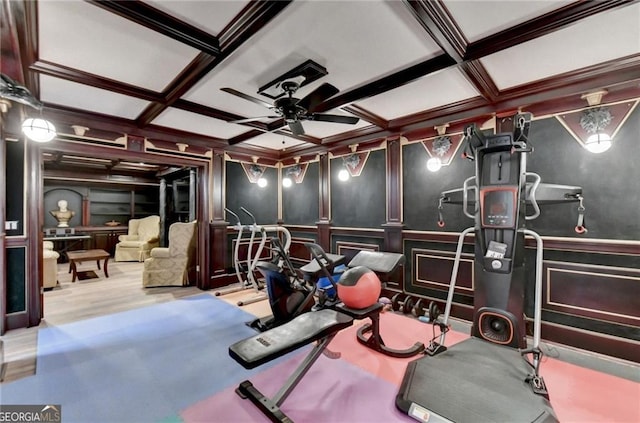 exercise area featuring coffered ceiling, a decorative wall, a wainscoted wall, ceiling fan, and crown molding