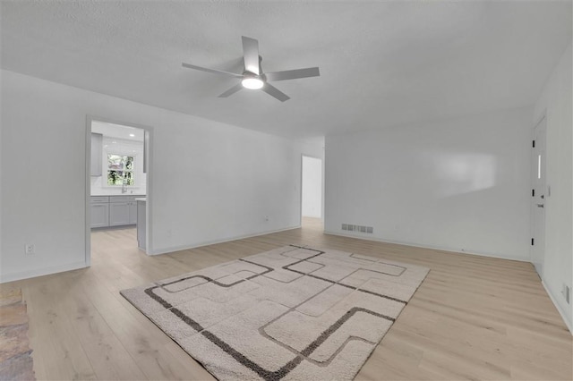 unfurnished living room featuring light wood-style flooring, a textured ceiling, a ceiling fan, visible vents, and a sink