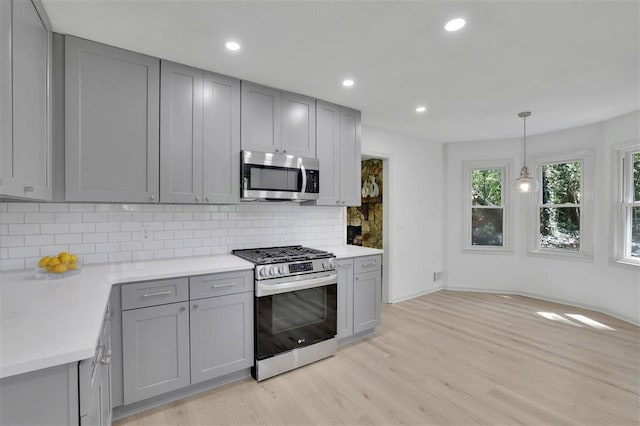 kitchen with tasteful backsplash, gray cabinets, light wood-style flooring, light countertops, and appliances with stainless steel finishes