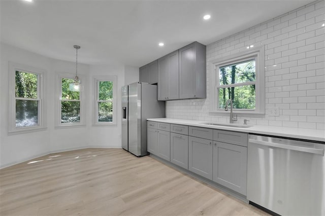 kitchen with light countertops, appliances with stainless steel finishes, a sink, and gray cabinetry