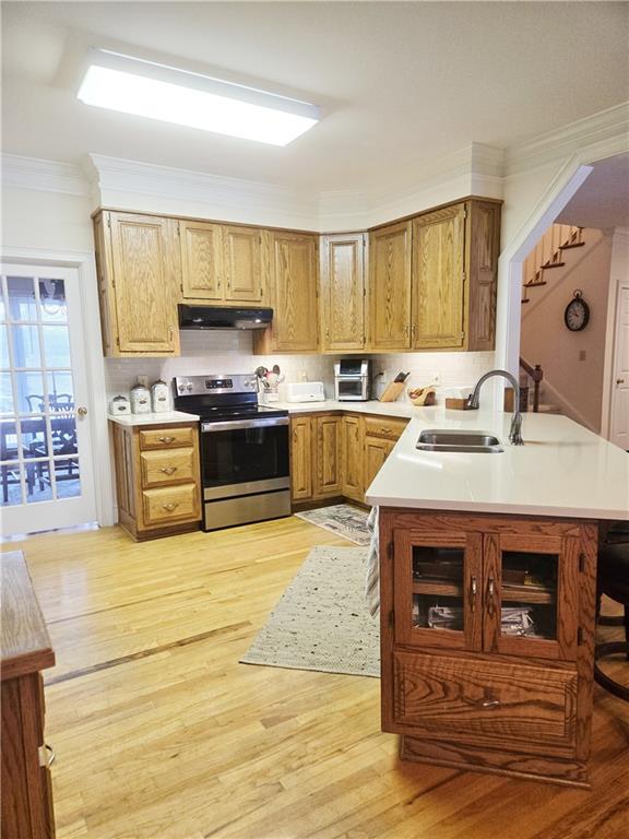 kitchen with stainless steel electric range oven, sink, ornamental molding, kitchen peninsula, and light hardwood / wood-style flooring