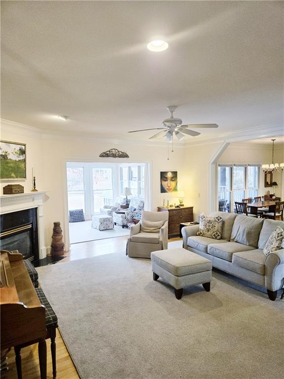 living room with a healthy amount of sunlight, ornamental molding, ceiling fan with notable chandelier, and light hardwood / wood-style flooring