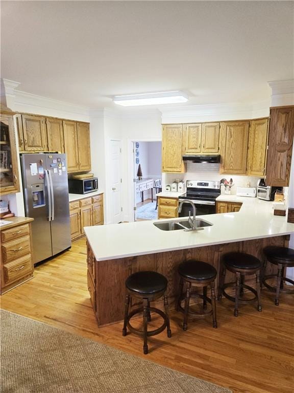 kitchen with a breakfast bar, a sink, under cabinet range hood, stainless steel appliances, and light wood-style floors