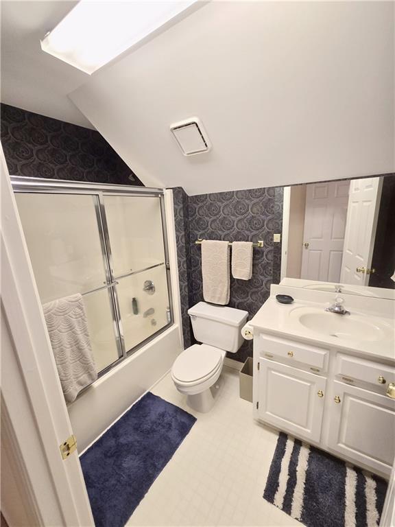 full bathroom with vanity, lofted ceiling, shower / bath combination with glass door, and toilet