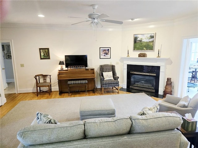 living room featuring crown molding, baseboards, a fireplace with flush hearth, wood finished floors, and a ceiling fan