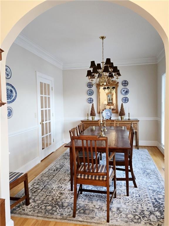 dining area featuring crown molding, baseboards, an inviting chandelier, wood finished floors, and arched walkways