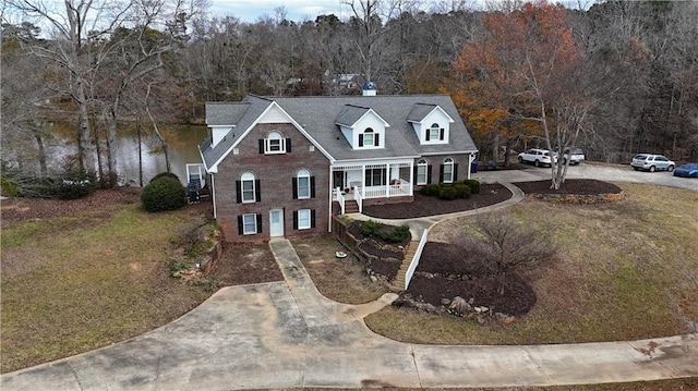 view of front facade featuring a forest view, covered porch, brick siding, and driveway