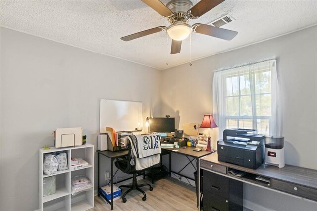 office with light wood finished floors, visible vents, a textured ceiling, and ceiling fan