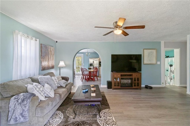 living area featuring a ceiling fan, baseboards, wood finished floors, arched walkways, and a textured ceiling