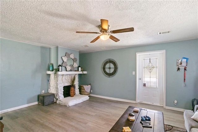 living area with visible vents, wood finished floors, a stone fireplace, baseboards, and ceiling fan