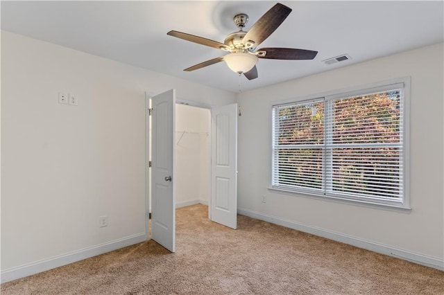 unfurnished bedroom with visible vents, a walk in closet, ceiling fan, baseboards, and light carpet