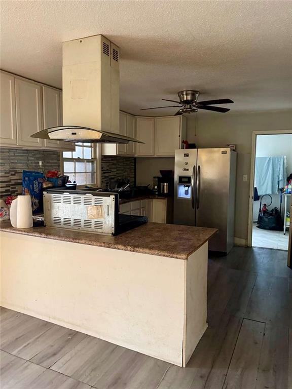 kitchen featuring white cabinets, stainless steel fridge, island exhaust hood, and a textured ceiling