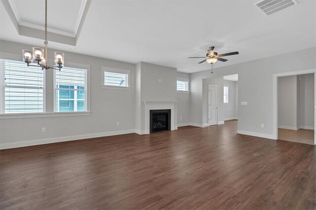 unfurnished living room with ceiling fan with notable chandelier, a raised ceiling, crown molding, and dark hardwood / wood-style flooring