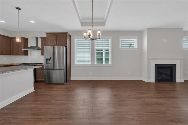 kitchen with stainless steel refrigerator with ice dispenser, wall chimney exhaust hood, hanging light fixtures, and dark hardwood / wood-style flooring