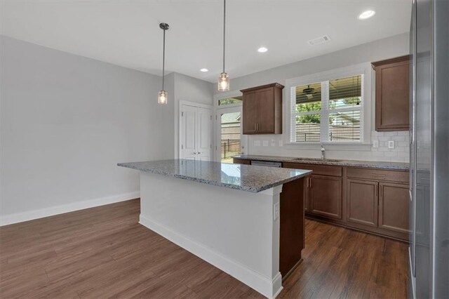 kitchen with sink, a kitchen island, decorative light fixtures, dark wood-type flooring, and light stone countertops