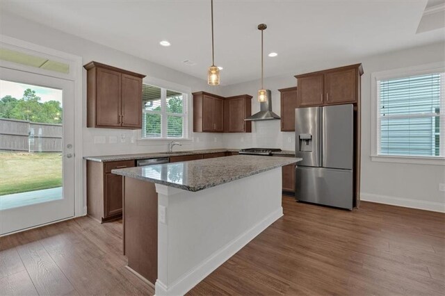 kitchen featuring a healthy amount of sunlight, stainless steel fridge, hardwood / wood-style floors, and wall chimney range hood