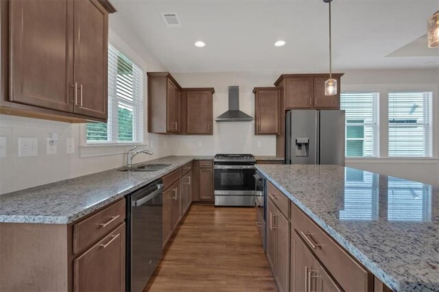 kitchen with pendant lighting, sink, wall chimney range hood, stainless steel appliances, and hardwood / wood-style floors