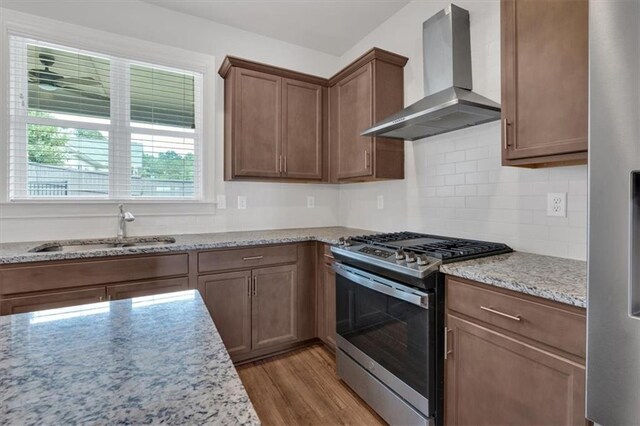 kitchen with light stone counters, stainless steel appliances, light hardwood / wood-style floors, and wall chimney range hood