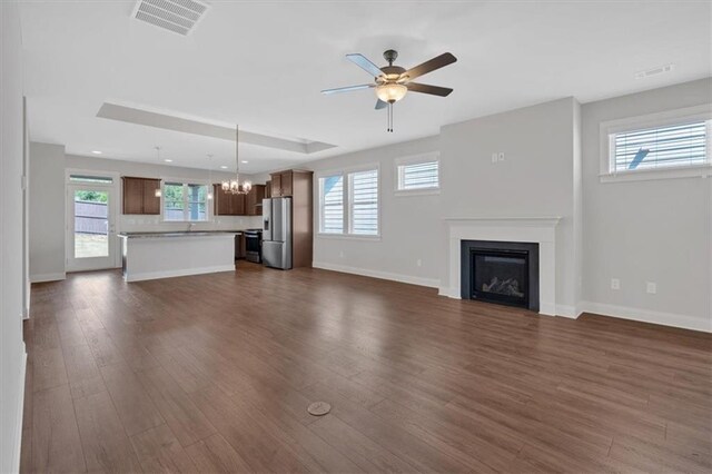 unfurnished living room with ceiling fan with notable chandelier, a wealth of natural light, and dark wood-type flooring