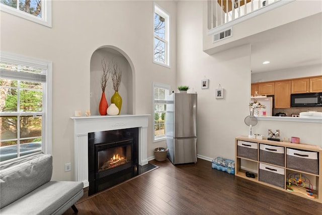 living area with dark wood finished floors, visible vents, a healthy amount of sunlight, and a glass covered fireplace