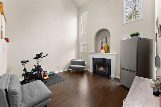 sitting room with dark wood-style floors, a fireplace with flush hearth, high vaulted ceiling, and baseboards