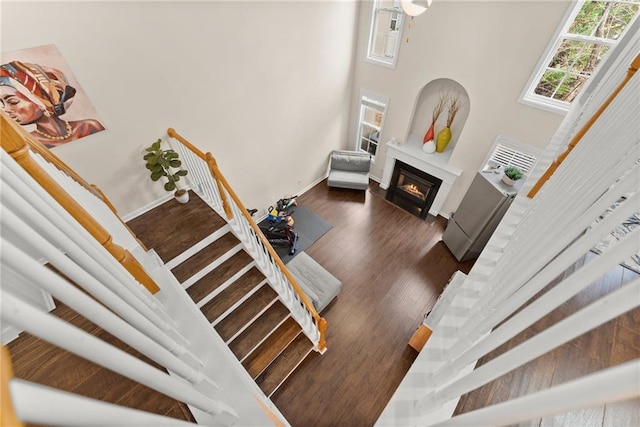 stairs featuring a glass covered fireplace, a towering ceiling, baseboards, and wood finished floors