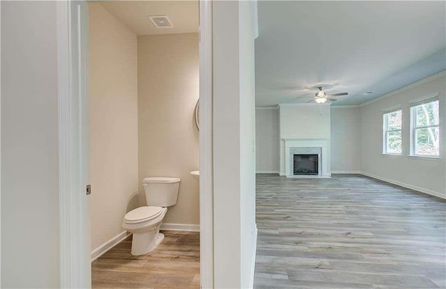 bathroom with toilet, crown molding, wood-type flooring, ceiling fan, and a fireplace