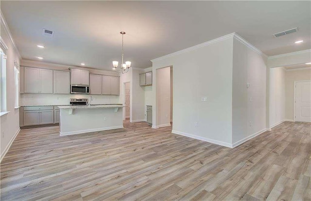 kitchen featuring pendant lighting, appliances with stainless steel finishes, gray cabinetry, light hardwood / wood-style floors, and a center island with sink