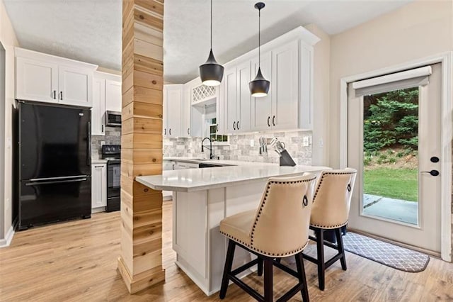 kitchen with a breakfast bar area, black appliances, decorative backsplash, white cabinets, and decorative light fixtures