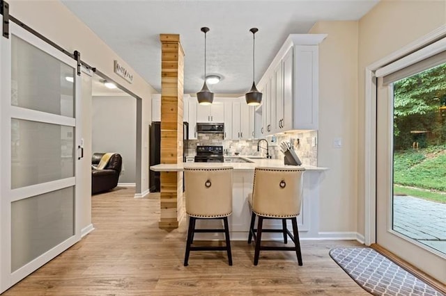 kitchen featuring a barn door, kitchen peninsula, a breakfast bar, electric range oven, and white cabinetry