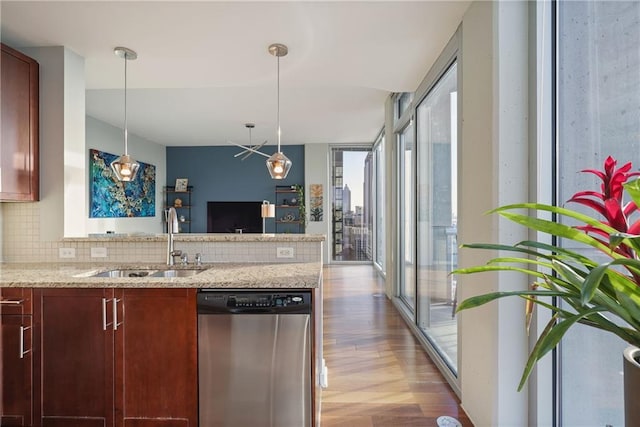 kitchen with light wood finished floors, a peninsula, a sink, stainless steel dishwasher, and tasteful backsplash