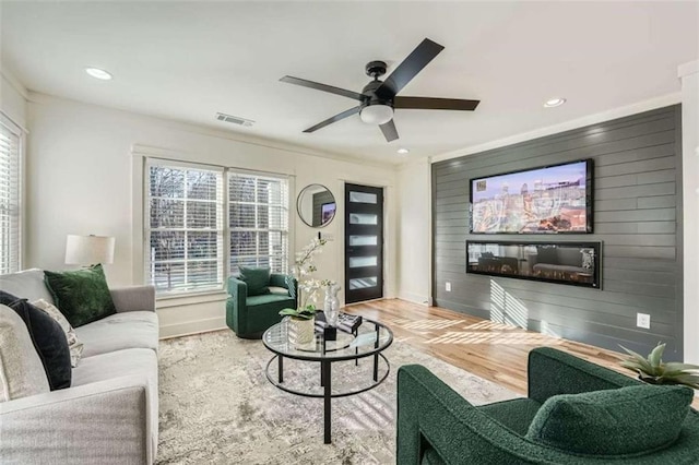 living room featuring hardwood / wood-style floors, ceiling fan, ornamental molding, and wood walls