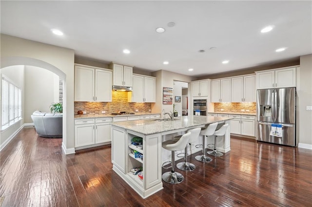 kitchen with under cabinet range hood, arched walkways, appliances with stainless steel finishes, and white cabinetry