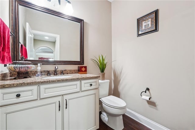 bathroom featuring toilet, vanity, baseboards, and wood finished floors