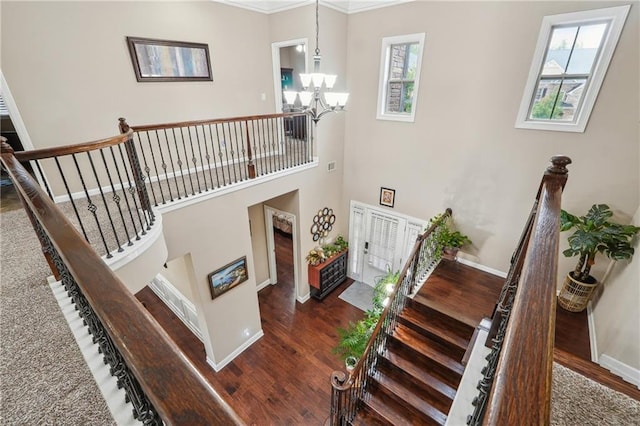 staircase with visible vents, wood finished floors, a towering ceiling, baseboards, and a chandelier