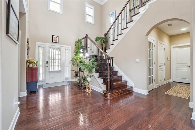 foyer entrance with visible vents, baseboards, stairway, wood finished floors, and arched walkways