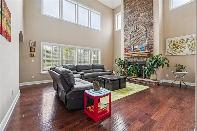 living room featuring baseboards, arched walkways, a stone fireplace, and hardwood / wood-style flooring