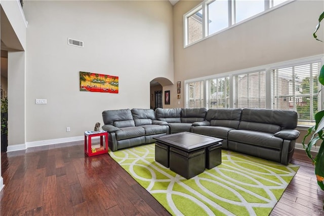 living area featuring visible vents, arched walkways, a high ceiling, wood-type flooring, and baseboards