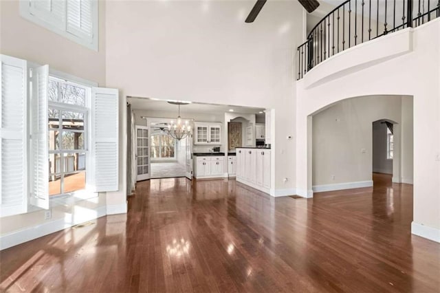 unfurnished living room with ceiling fan with notable chandelier, dark hardwood / wood-style flooring, and a high ceiling