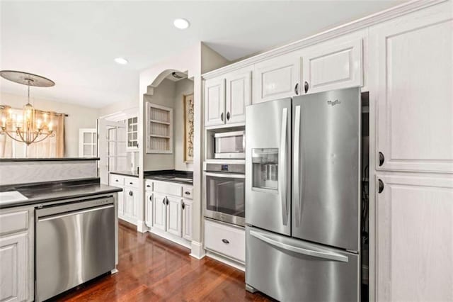 kitchen with appliances with stainless steel finishes, dark wood-style flooring, dark countertops, and an inviting chandelier