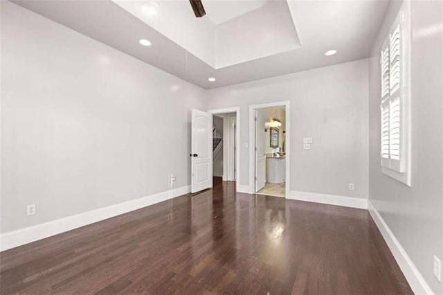 unfurnished bedroom featuring a tray ceiling, baseboards, ensuite bathroom, and wood finished floors