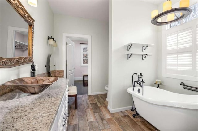 full bath featuring baseboards, a freestanding bath, toilet, vanity, and wood finished floors