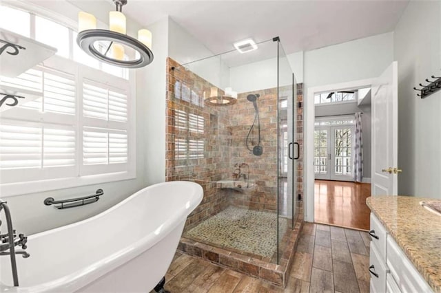 bathroom with a freestanding bath, a notable chandelier, a shower stall, vanity, and wood finished floors